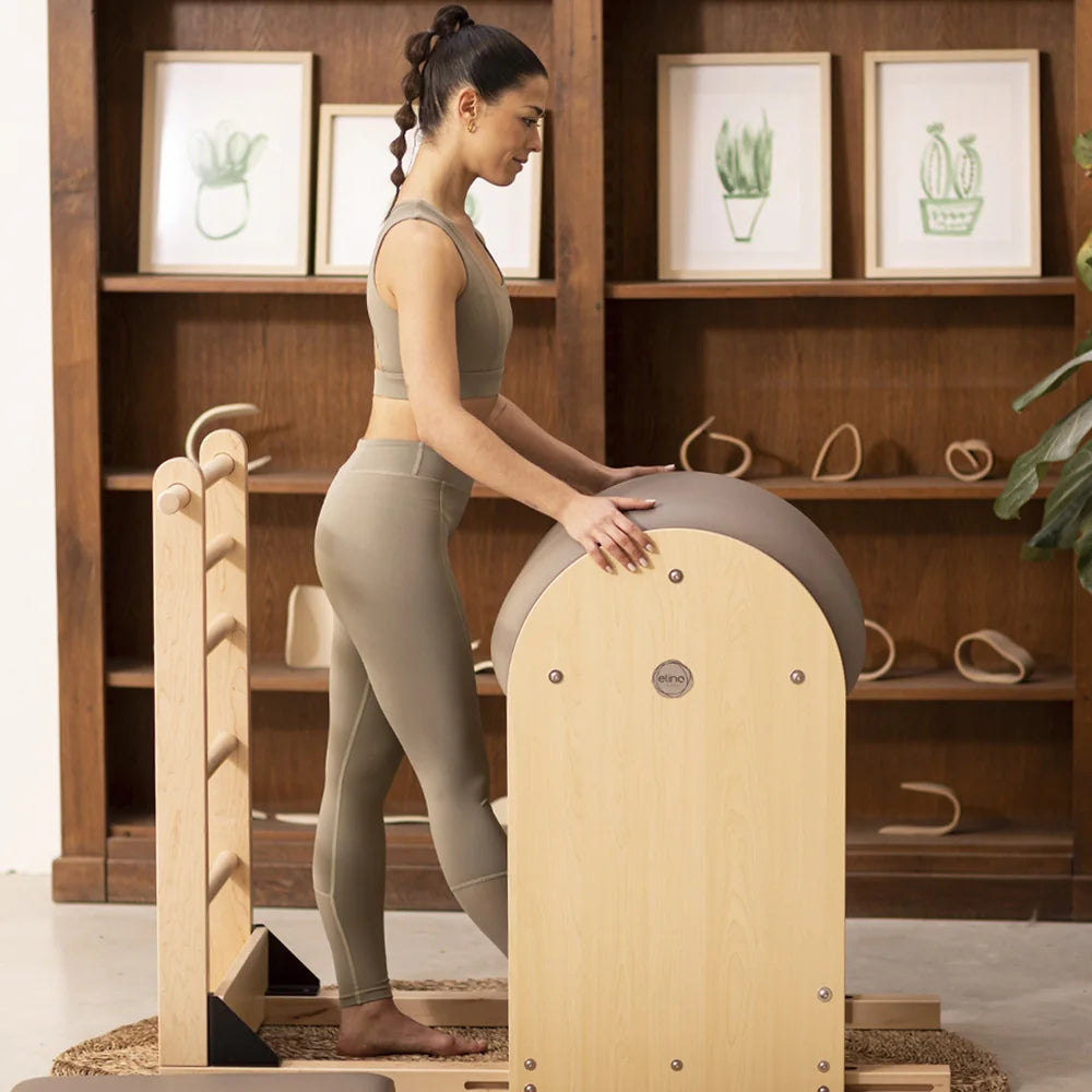 Woman performing a standing exercise on an Elina Pilates wooden base Ladder Barrel