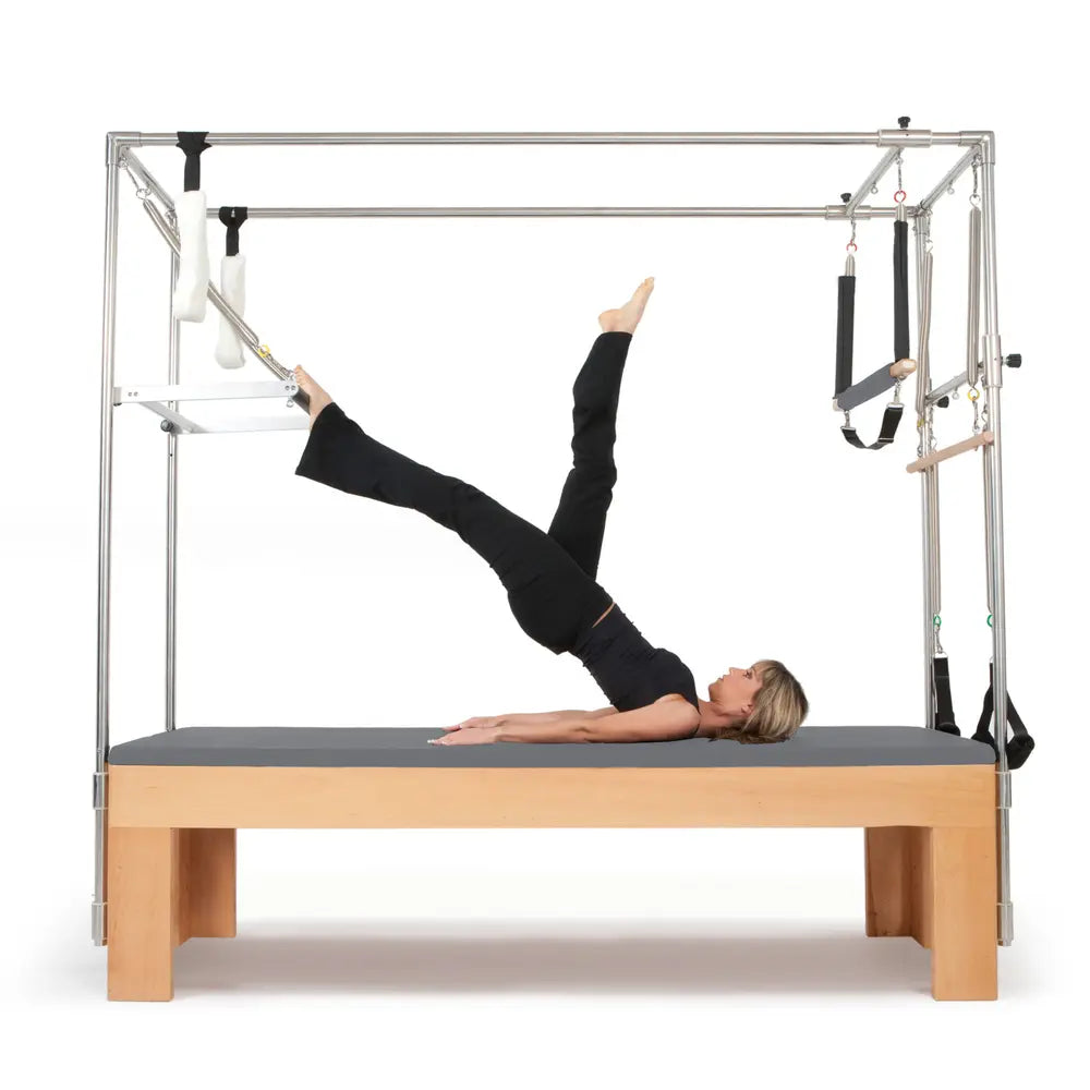 Woman performing a leg lift exercise on the grey Elina Pilates Wooden Cadillac