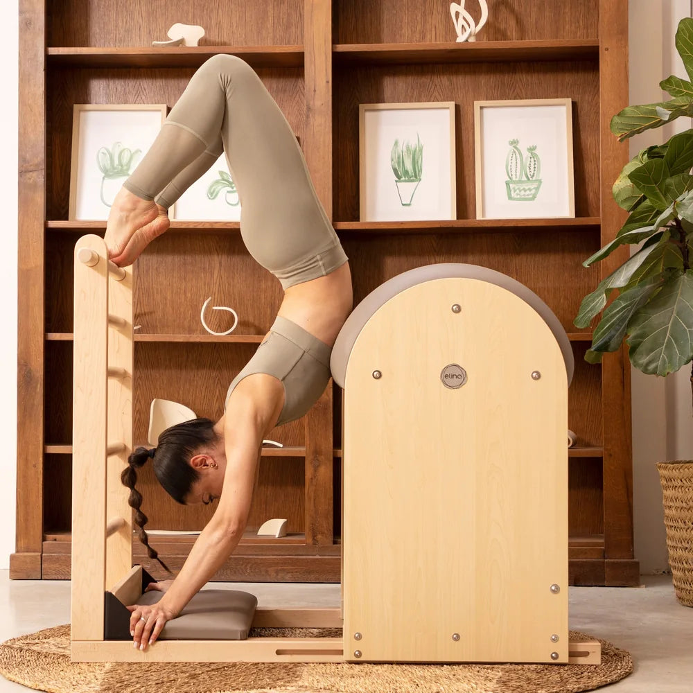 Woman performing an inverted exercise on an Elite Elina Pilates wooden base Ladder Barrel