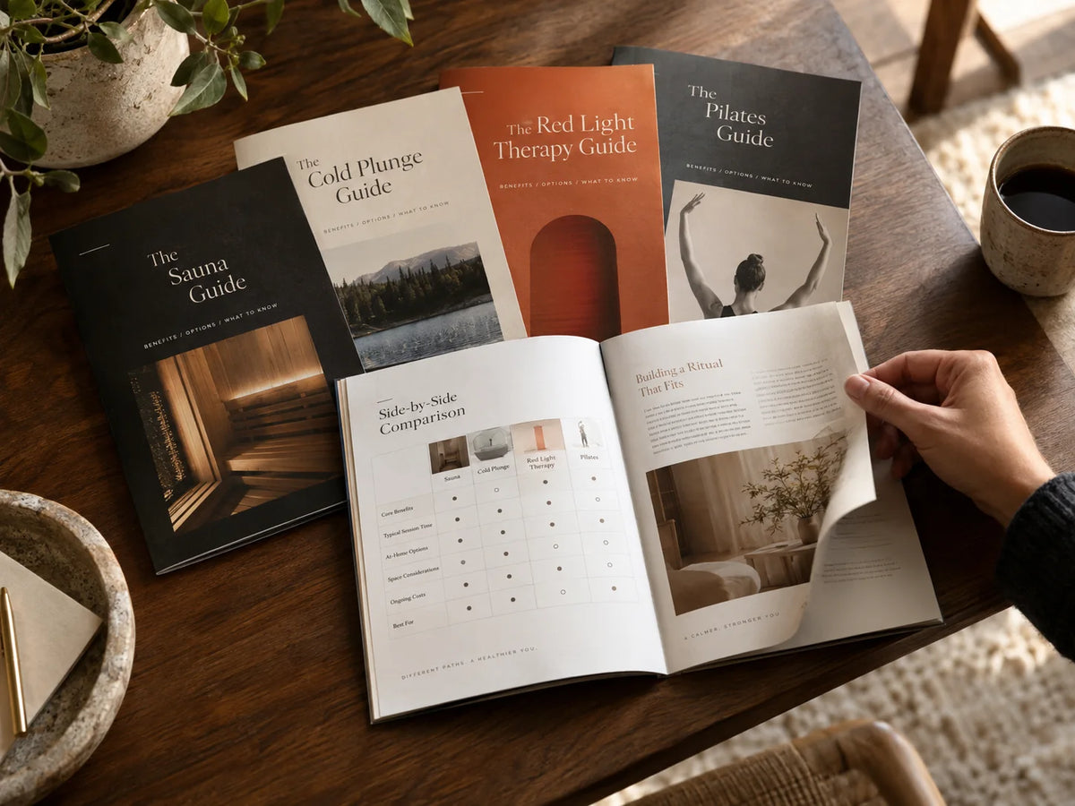 A collection of Kinaura buying guides for saunas, cold plunges, red light therapy, and Pilates on a wooden table.
