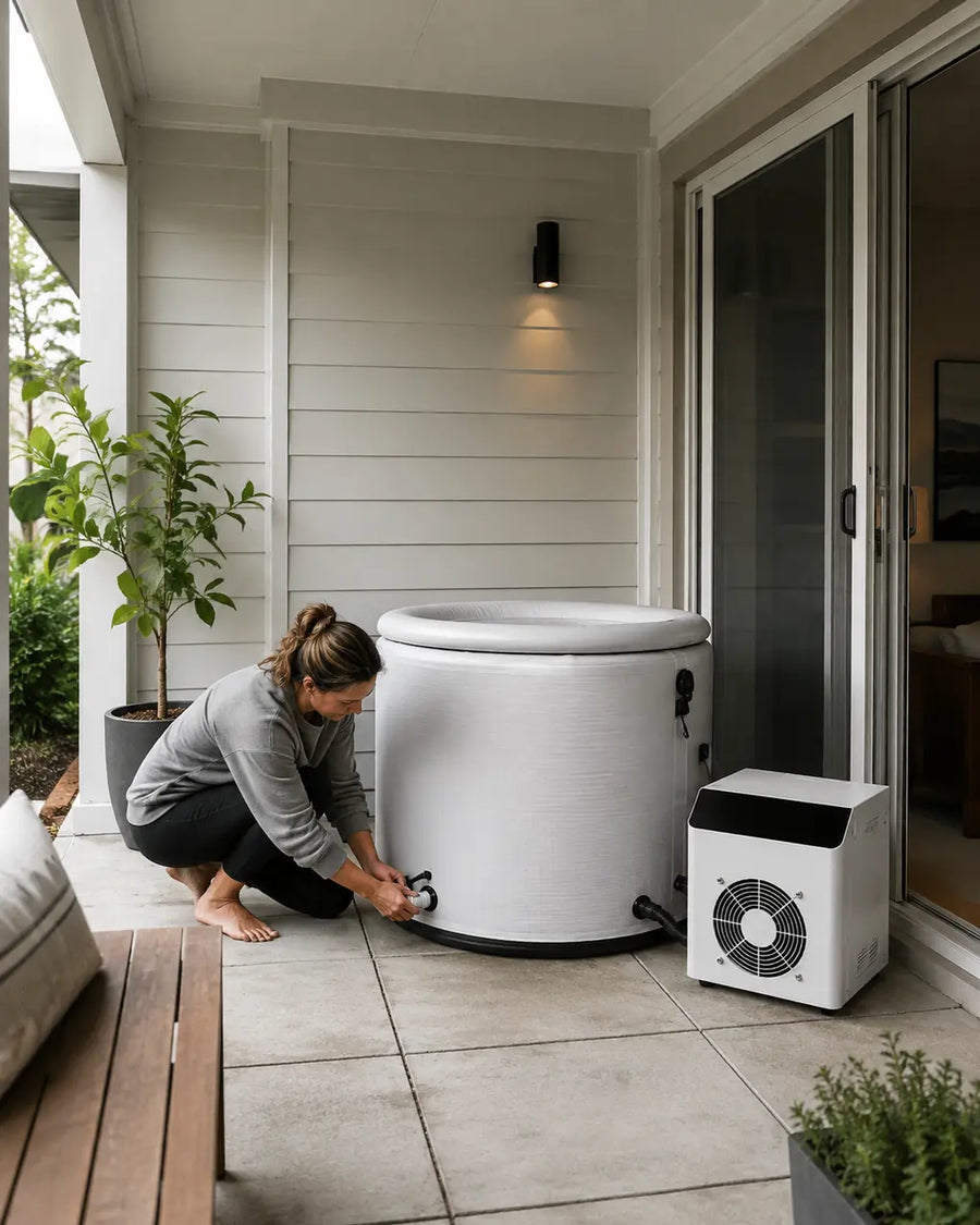 Woman connecting a hose to a compact inflatable cold plunge pod on a covered patio.