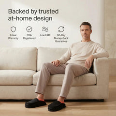 Man on a sofa wearing Nicebeam Red Light Therapy Slippers with warranty and at-home use icons