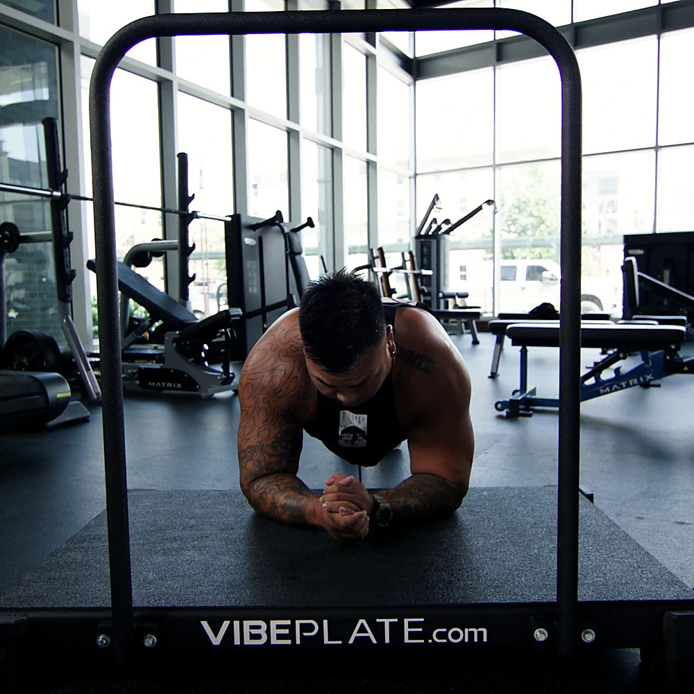 Man holding a plank on the VibePlate 3048 with balance bar in a gym