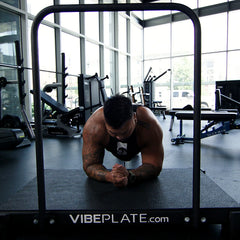 Man holding a plank on the VibePlate 3048 with balance bar in a gym